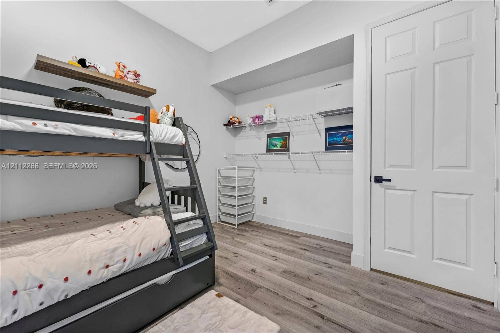 Wood-finish flooring, white four-panel interior door with matte black hardware, and built-in white wire shelving system