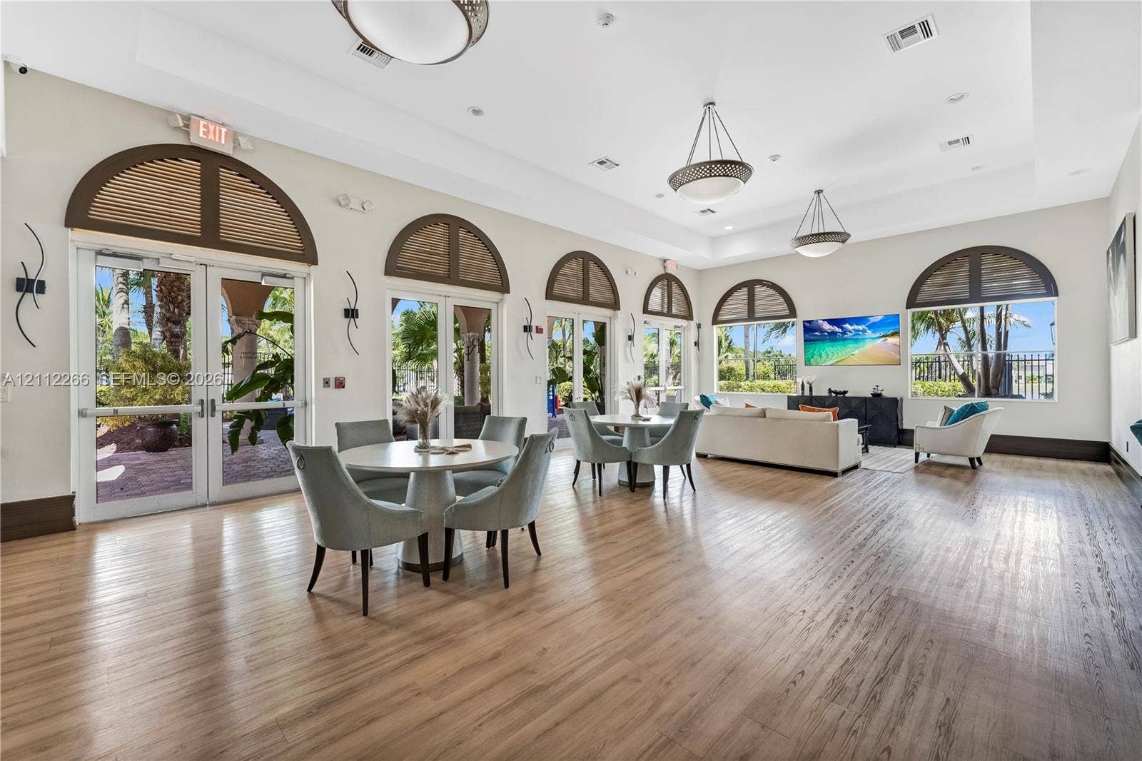 Spacious common area featuring wood-finish flooring, tray ceilings, multiple arched glass entryways with transom windows, and recessed lighting