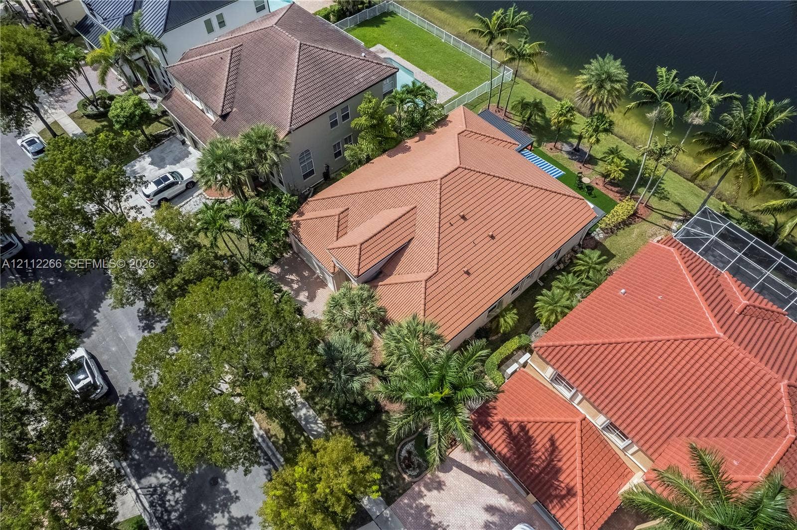 Aerial perspective featuring a tile roof, paved driveway, mature landscaping, and water frontage
