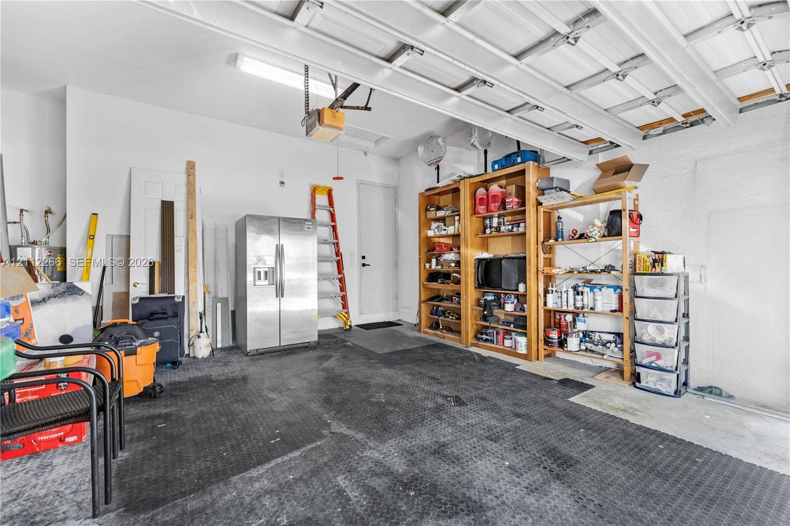Garage space featuring high-reaching ceiling, overhead linear lighting, interior pedestrian door, and durable rubber flooring
