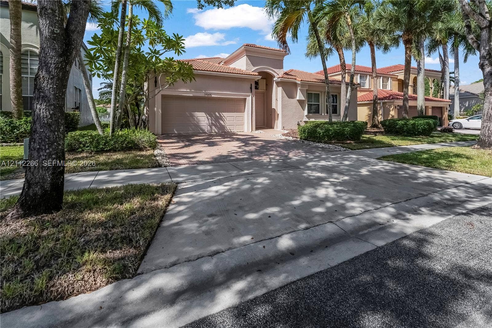 Stucco exterior featuring a clay tile roof, arched entryway, paved driveway, and attached two-car garage