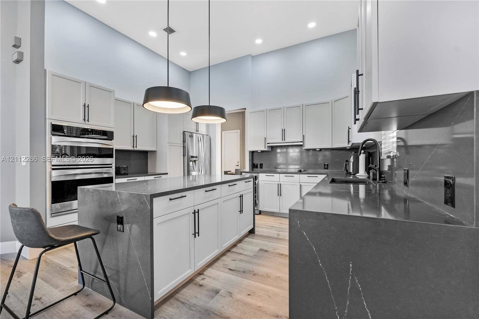 Kitchen featuring a waterfall-edge island, dark stone-finish countertops, ceiling-height cabinetry, double wall ovens, and wood-finish flooring
