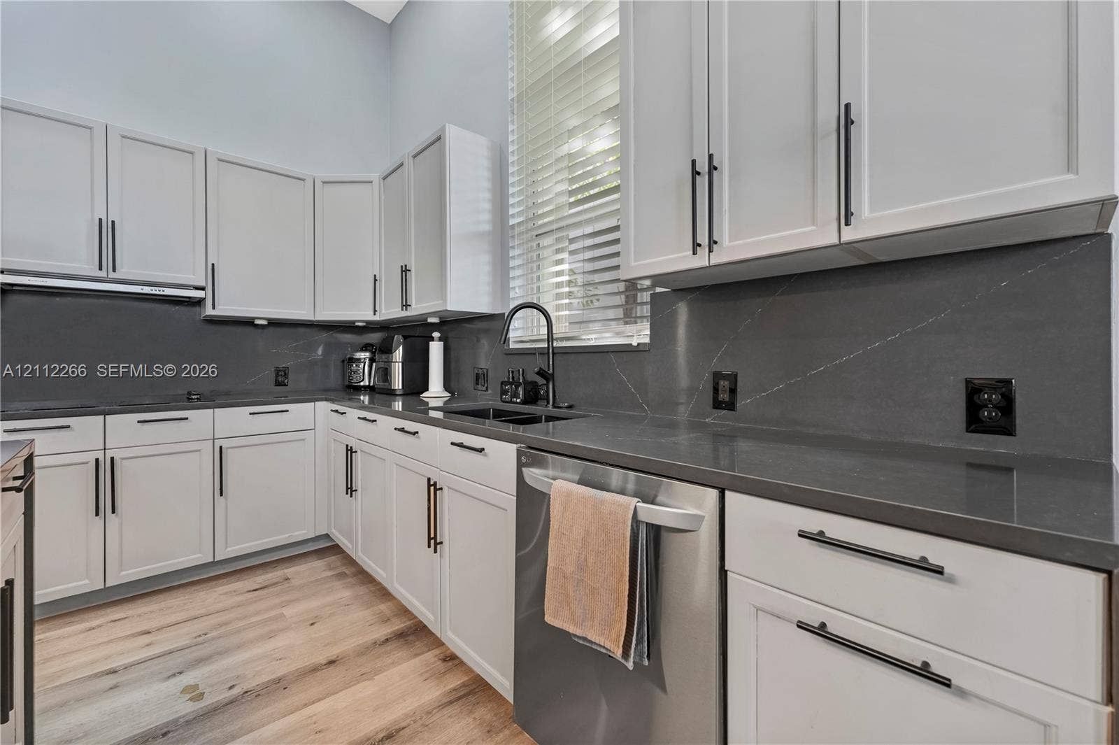 Kitchen featuring white shaker-style cabinetry, dark stone countertops, stainless steel dishwasher, matte black hardware, and wood-finish flooring