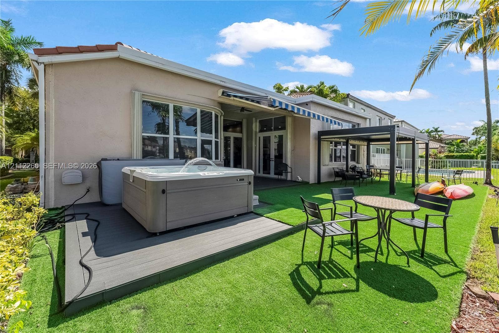 Rear exterior featuring an integrated spa, elevated composite decking, a fixed metal-frame pergola, and artificial turf landscaping