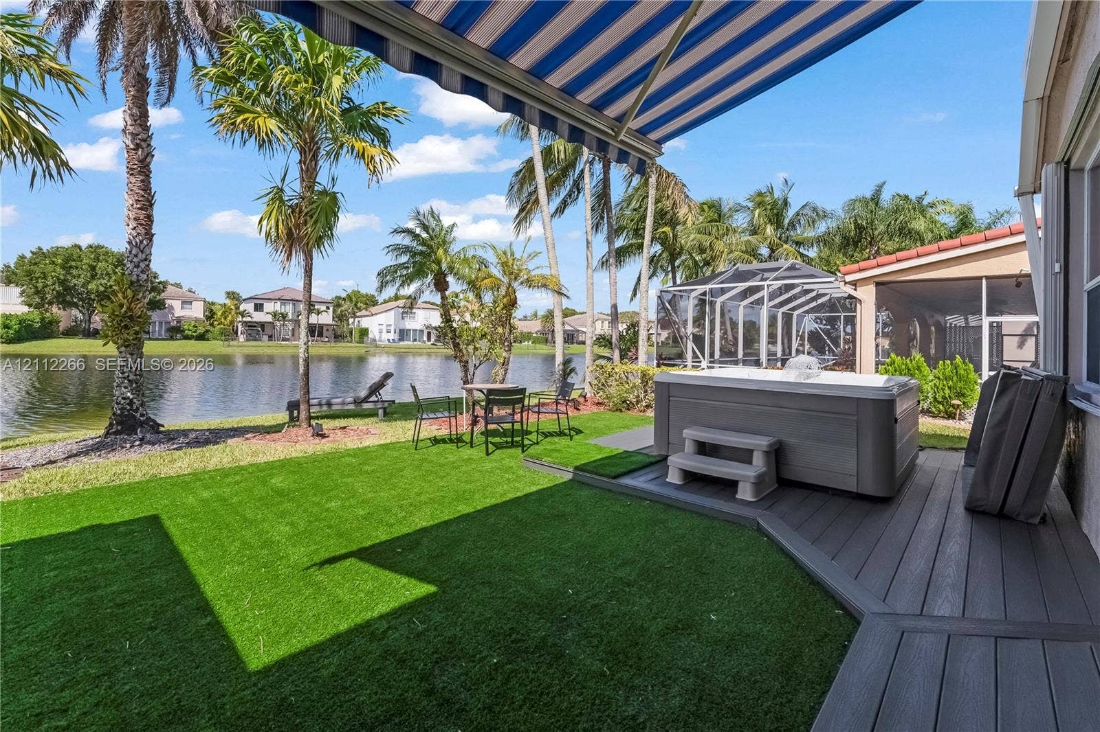 Waterfront backyard featuring synthetic turf, a built-in spa, a multi-level composite deck, and a retractable fabric awning