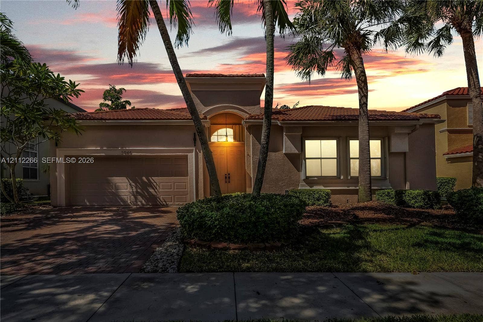 Stucco exterior residence featuring a tile roof, arched entryway, multi-panel garage door, and mature landscaping