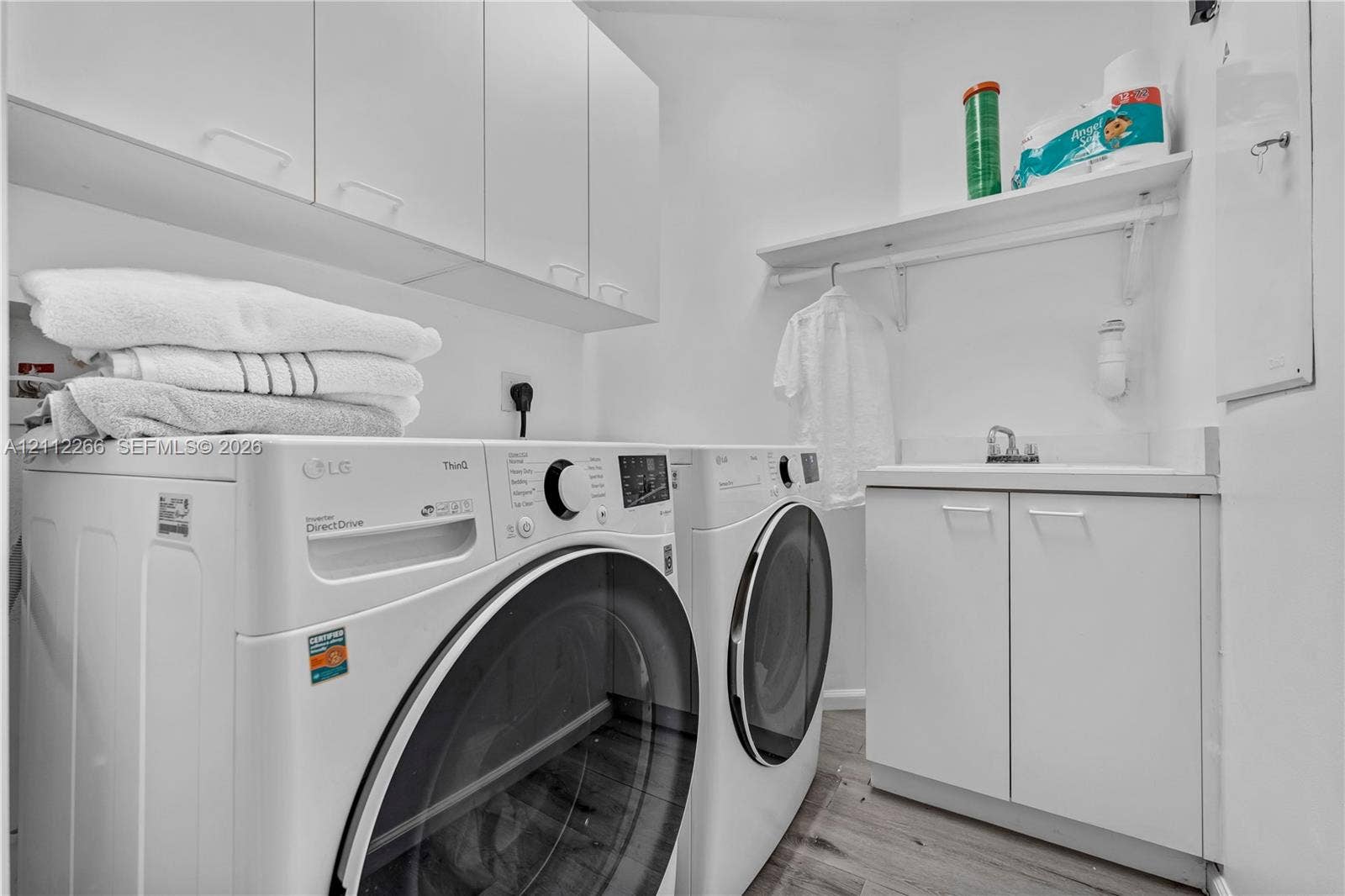 Laundry area featuring white cabinetry, integrated sink, wood-finish flooring, and built-in shelving with a clothes rod