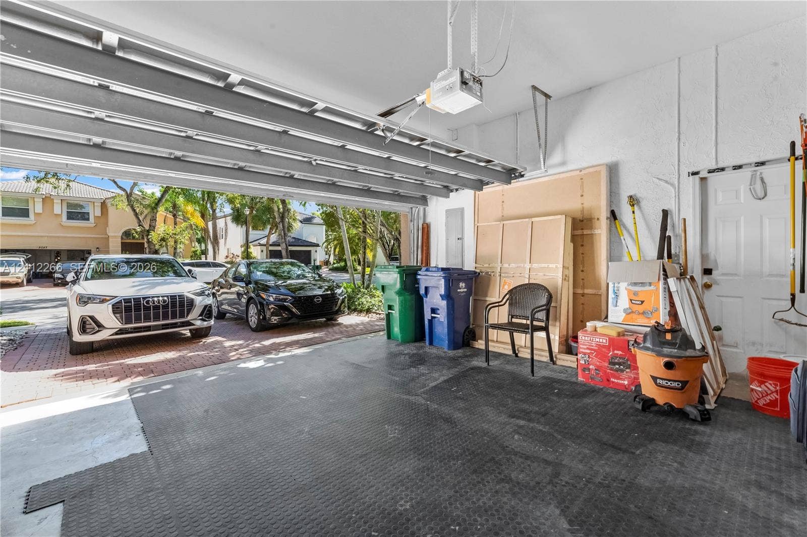 Two-car garage featuring a motorized overhead door, durable flooring, integrated ceiling-mounted door opener, and a dedicated pedestrian access door