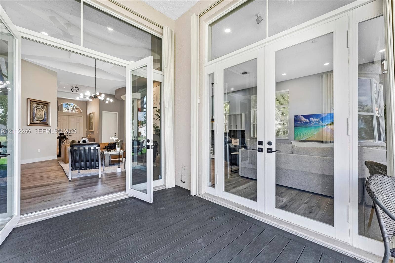 Covered patio featuring charcoal-tone composite decking and double glass-paneled entry doors with transom windows