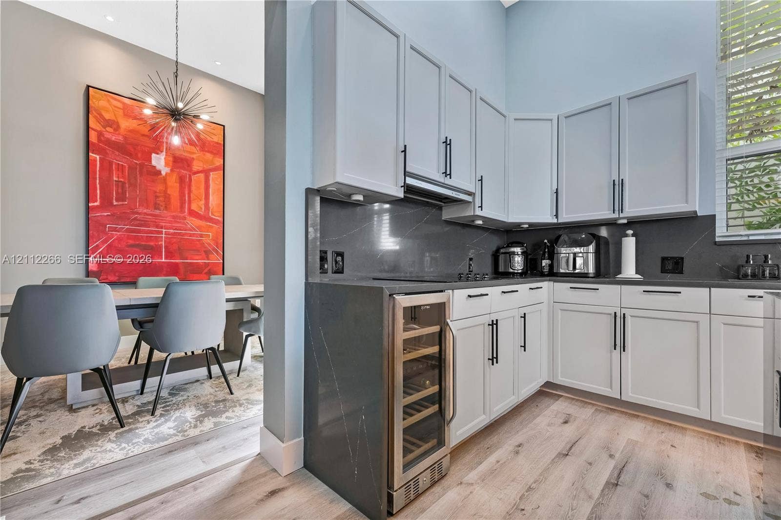 Kitchen featuring white shaker-style cabinetry, charcoal stone countertops, integrated wine refrigerator, and light wood-finish flooring