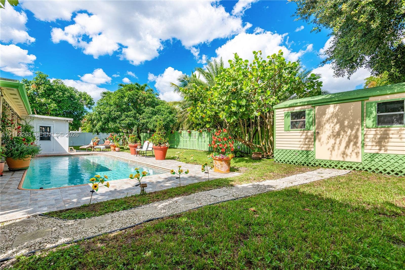 5941 SW 16th Court, Plantation, FL 33317 Backyard featuring a concrete-paver patio, swimming pool, detached storage structure, manicured lawn, and perimeter lattice fencing