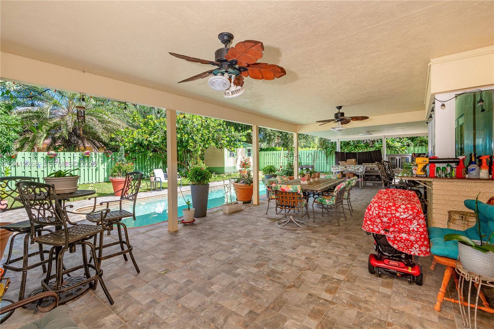 5941 SW 16th Court, Plantation, FL 33317 Covered outdoor patio featuring tile flooring, ceiling fans with light fixtures, and a recessed service counter with brick masonry