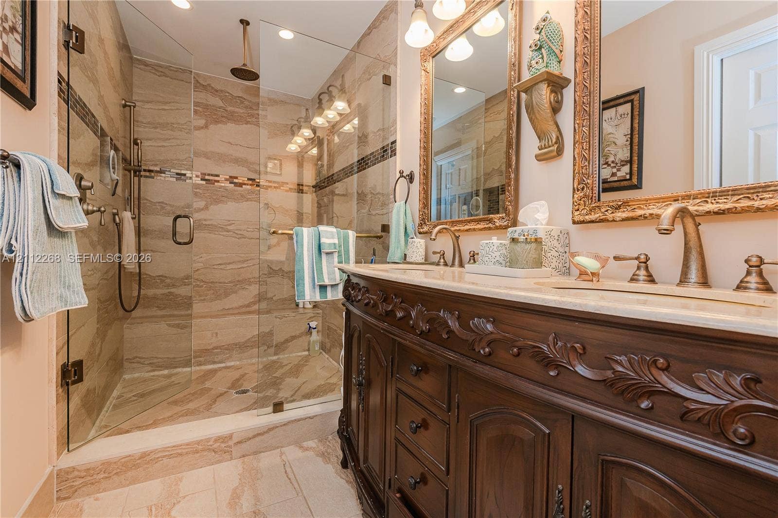 5941 SW 16th Court, Plantation, FL 33317 Bathroom featuring an expansive wood vanity with intricate carved detailing, a glass-enclosed walk-in shower with floor-to-ceiling tile surround, stone-finish countertops, dual-sink configuration, and brass-tone plumbing fixtures