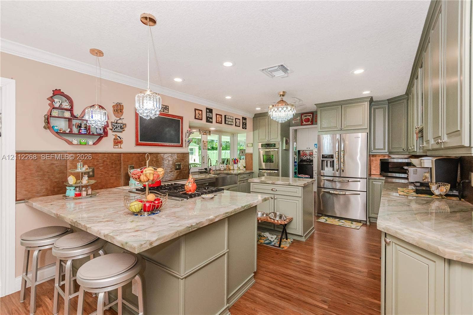 5941 SW 16th Court, Plantation, FL 33317 Kitchen featuring sage-toned cabinetry, stone-finish countertops, stainless steel appliances, wood-finish flooring, and multi-light crystal pendant fixtures