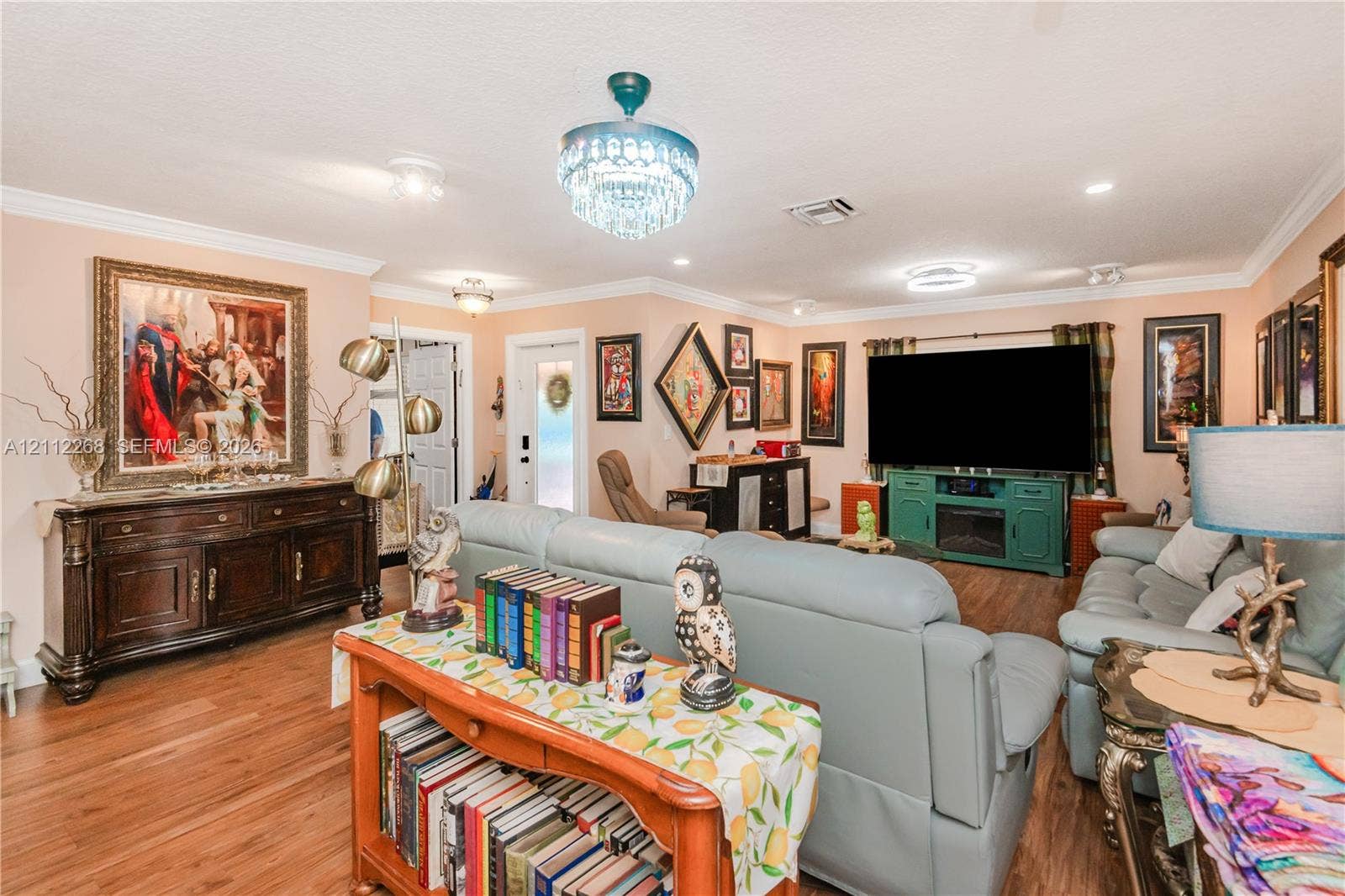 5941 SW 16th Court, Plantation, FL 33317 Living area featuring wood-finish flooring, a tiered crystal chandelier, crown molding, and a front entry door with a decorative glass insert