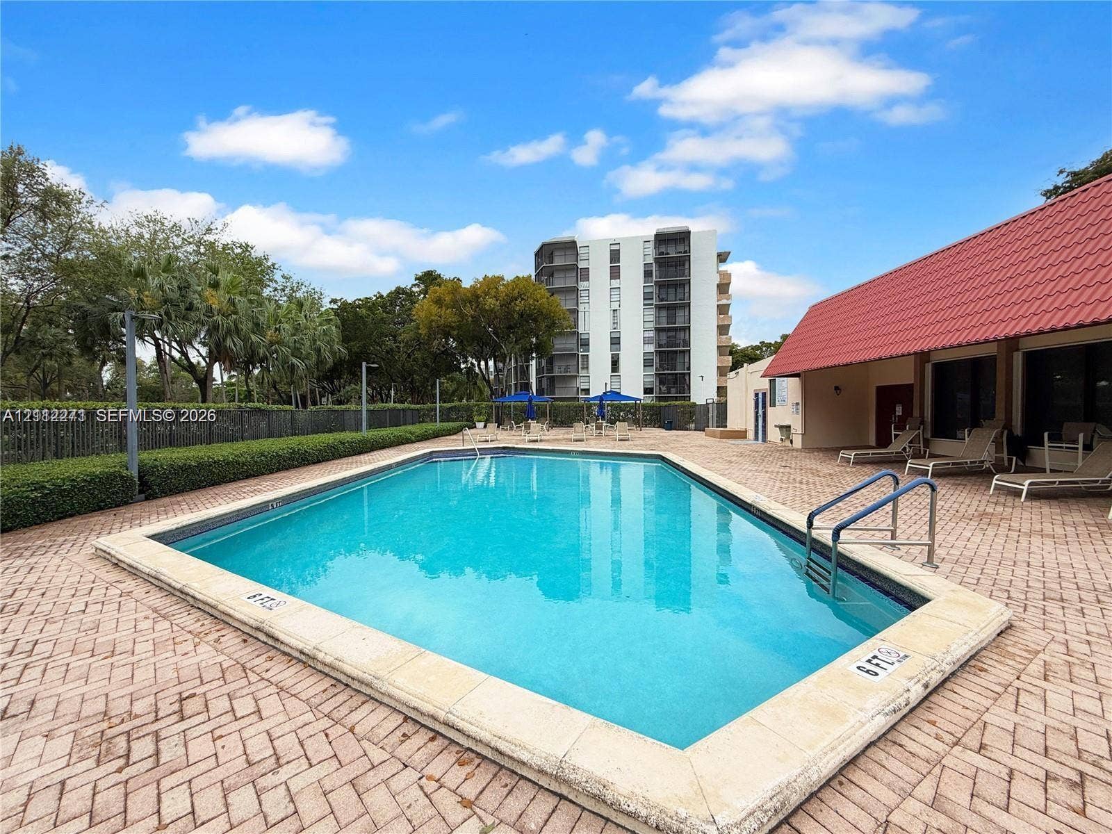 Rectangular swimming pool featuring a stone coping edge, metallic handrails, and a surrounding herringbone-patterned brick deck