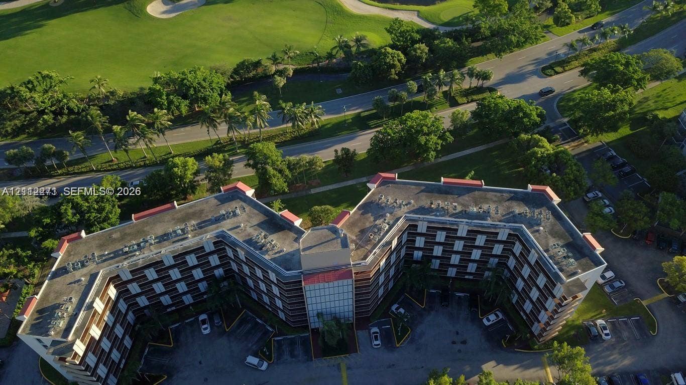 Aerial perspective of a multi-story building with a red-tiled roofline, featuring surface parking, lush greenery, and integrated palm landscaping