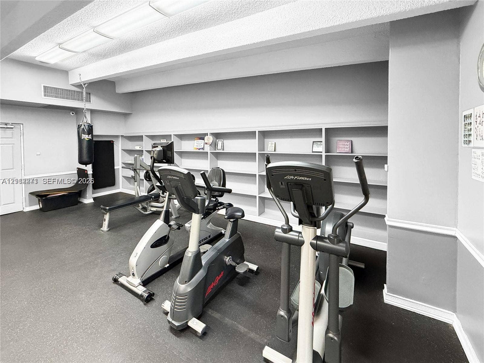Fitness area featuring wall-to-wall built-in shelving, resilient rubber flooring, and recessed ceiling lighting