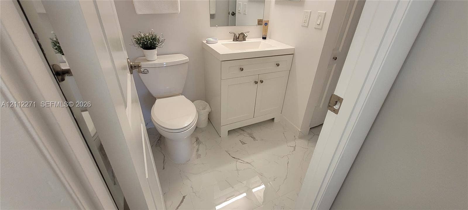 Bathroom featuring a white vanity cabinet with a integrated sink, polished stone-finish flooring with vein detailing, a dual-flush toilet, and a wall-mounted mirror