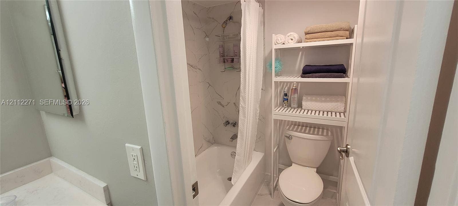 Bathroom featuring a tub-shower combination with floor-to-ceiling stone-patterned wall surround, a wall-mounted mirror, and a solid-surface vanity countertop