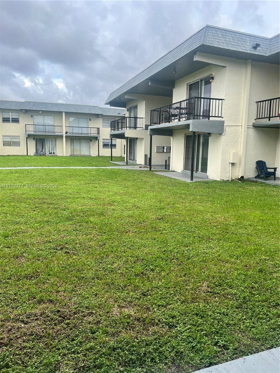301 NW 177th Street, #141, Miami Gardens, FL 33169 Exterior facade featuring stucco siding, elevated balconies with metal railings, sliding glass doors, and expansive grassy grounds