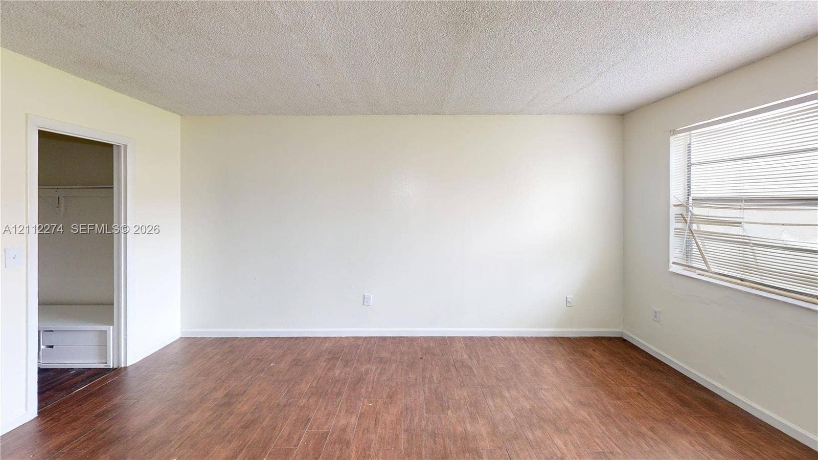 301 NW 177th Street, #141, Miami Gardens, FL 33169 Neutral-toned interior space featuring wood-finish flooring, textured ceiling, and a closet with built-in shelving