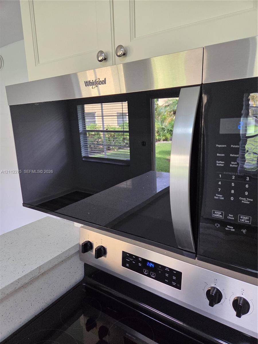 Stainless steel over-the-range microwave, smooth-top electric range, light-toned shaker-style cabinetry, and quartz countertops with integrated fleck detailing