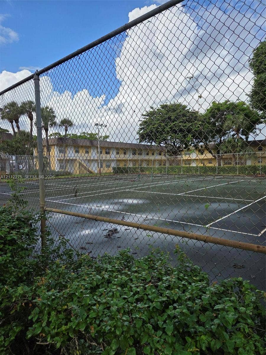 Tennis court with chain-link fencing, surrounded by mature trees and palms