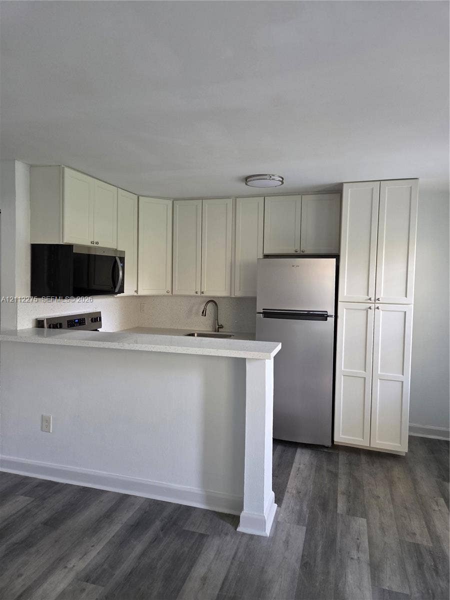 Kitchen featuring white shaker-style cabinetry, a stone-finish countertop with an integrated breakfast bar, stainless steel appliances, and wood-finish flooring