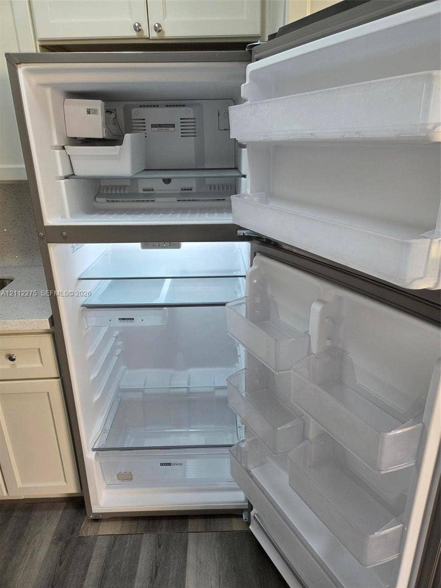 Stainless steel top-freezer refrigerator featuring an integrated ice maker, adjustable glass shelving, clear produce drawers, and interior LED lighting