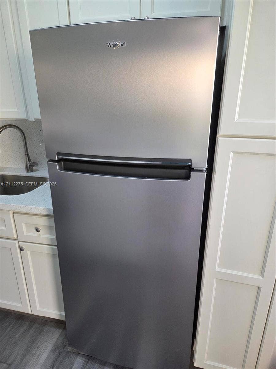 Stainless steel top-freezer refrigerator, white shaker-style cabinetry, solid-surface countertop, and stainless steel sink with a high-arch faucet