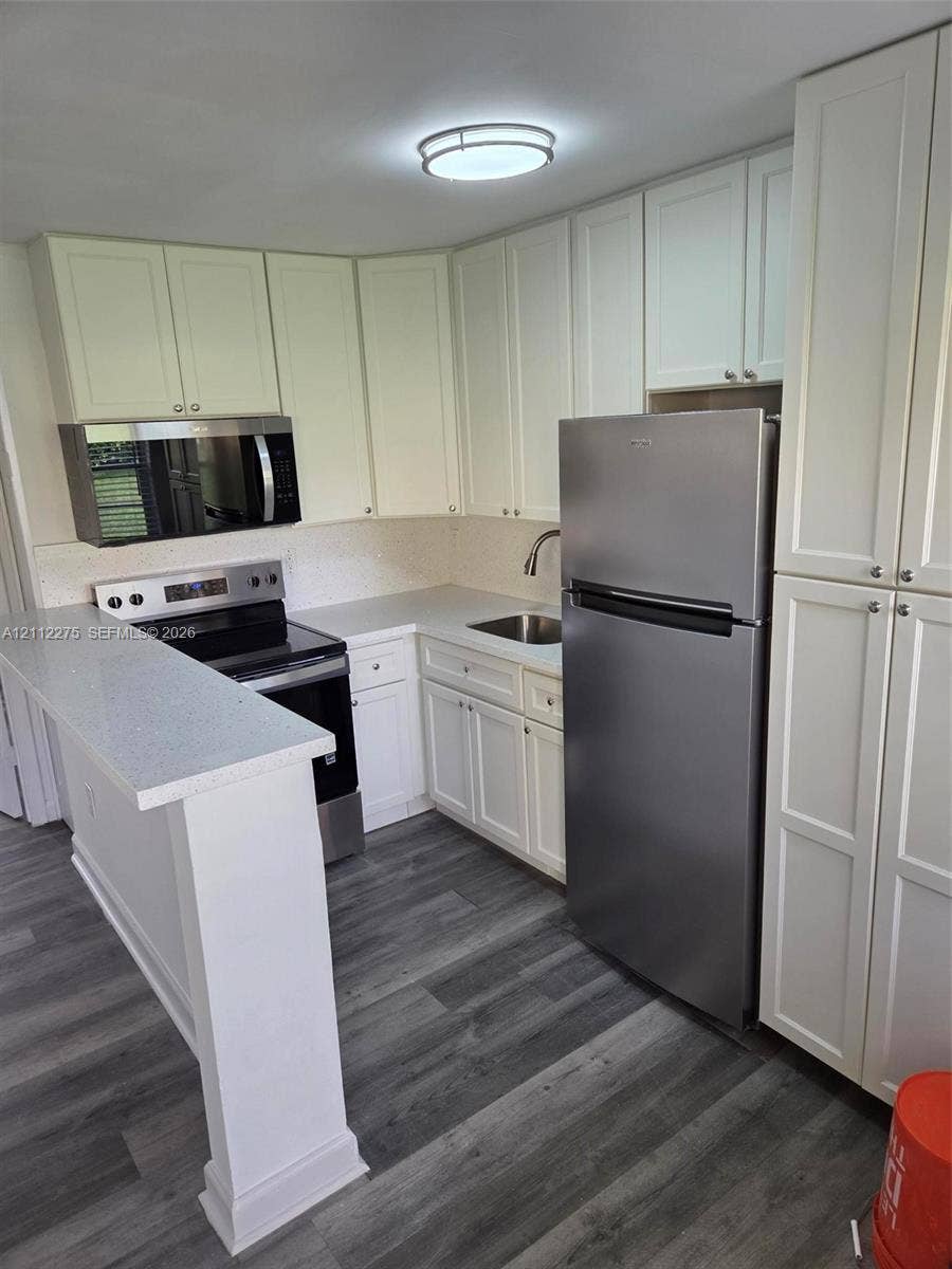 Kitchen featuring white cabinetry, quartz countertops, stainless steel appliances, and wood-finish flooring