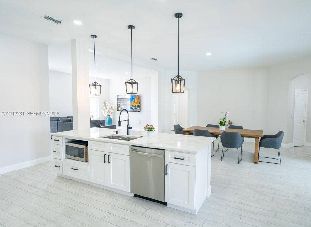 2461 Winfield, Kissimmee, FL 34743 Kitchen island featuring white shaker-style cabinetry, quartz countertops, a stainless steel dishwasher, an undermount sink with a matte black faucet, and three pendant lights