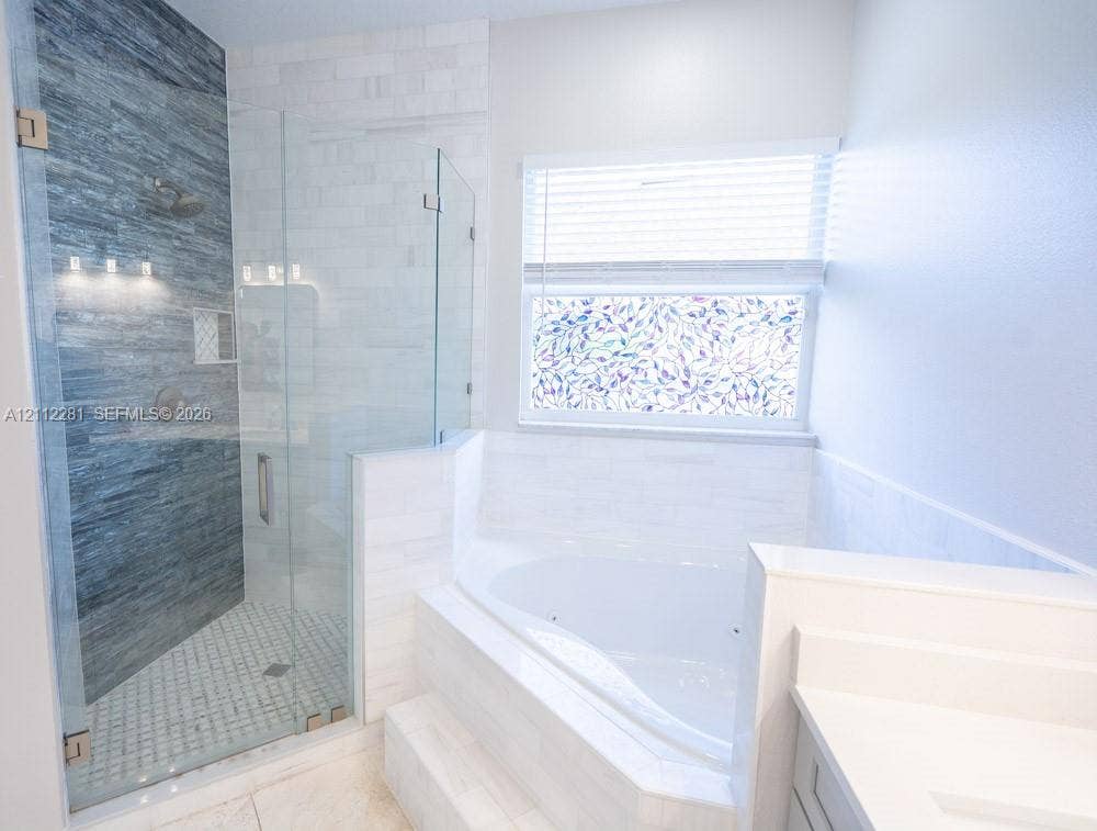 2461 Winfield, Kissimmee, FL 34743 Walk-in glass-enclosed shower with horizontal textured tiling and built-in shelving, alongside a white jetted soaking tub with tile surround