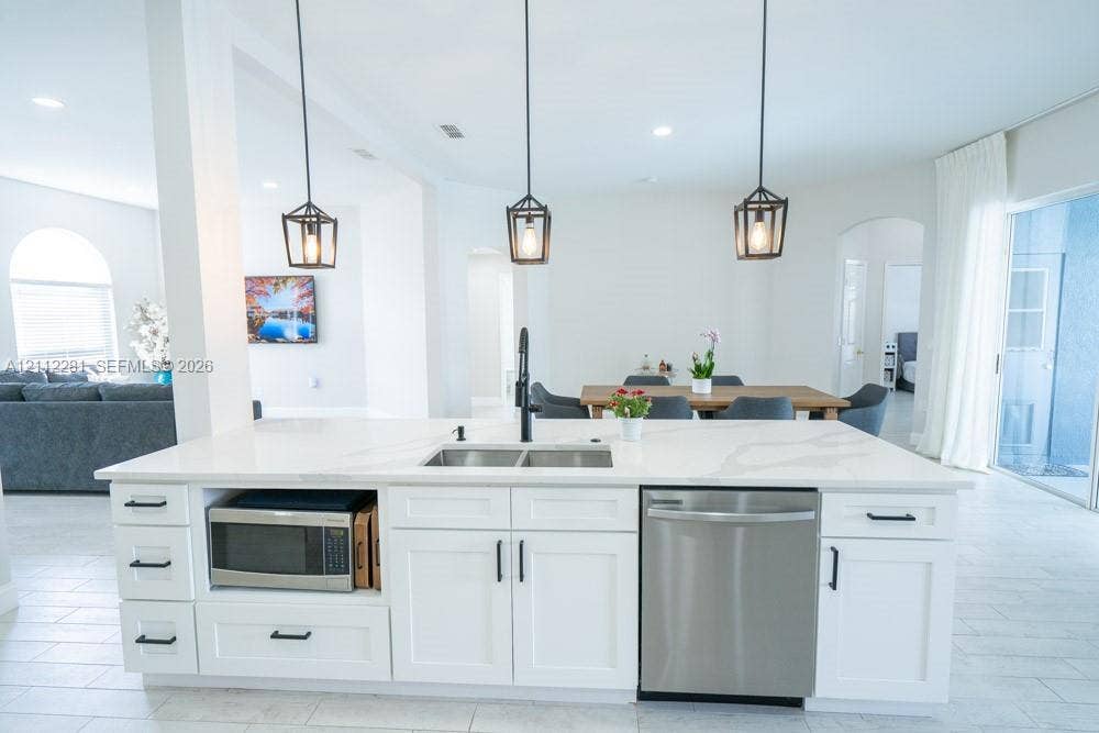 2461 Winfield, Kissimmee, FL 34743 Kitchen island featuring stone-look countertops, white shaker-style cabinetry, matte black hardware, three geometric pendant lights, and a stainless steel undermount sink with a high-arch faucet