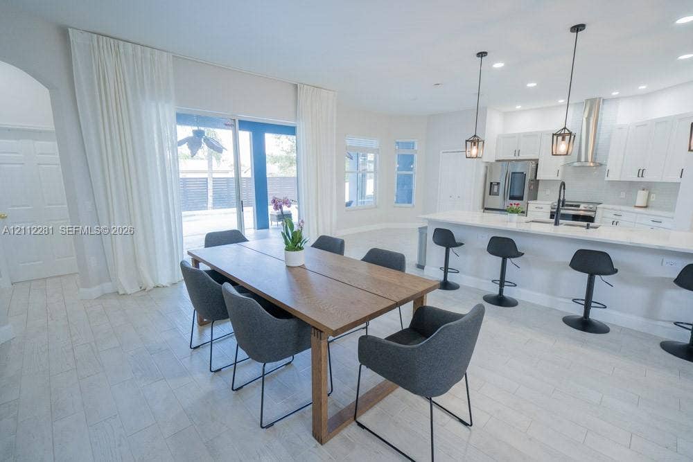 2461 Winfield, Kissimmee, FL 34743 Open-concept kitchen featuring white shaker-style cabinetry, quartz countertops, a stainless steel range hood, pendant lighting, and wood-finish tile flooring