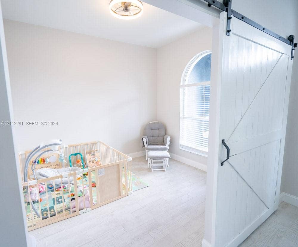 2461 Winfield, Kissimmee, FL 34743 Flexible office/den featuring a white sliding barn door, arched window, wood-finish flooring, and a modern flush-mount ceiling light