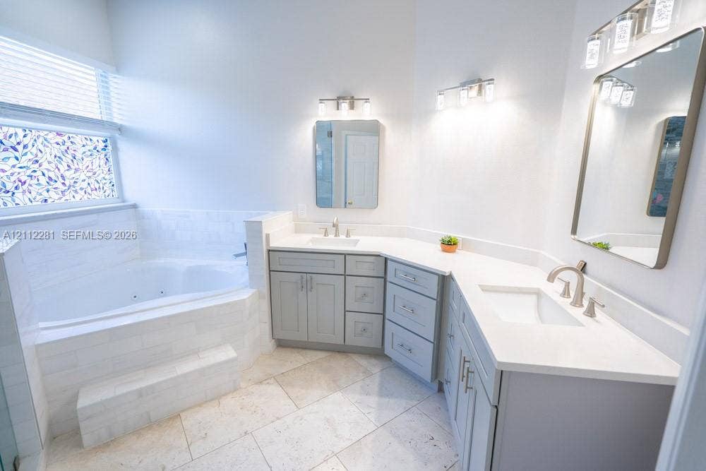 2461 Winfield, Kissimmee, FL 34743 Bathroom featuring a corner soaking tub with a tiled surround, dual-sink vanity with light-colored cabinetry, stone-finish flooring, and wall-mounted vanity lighting