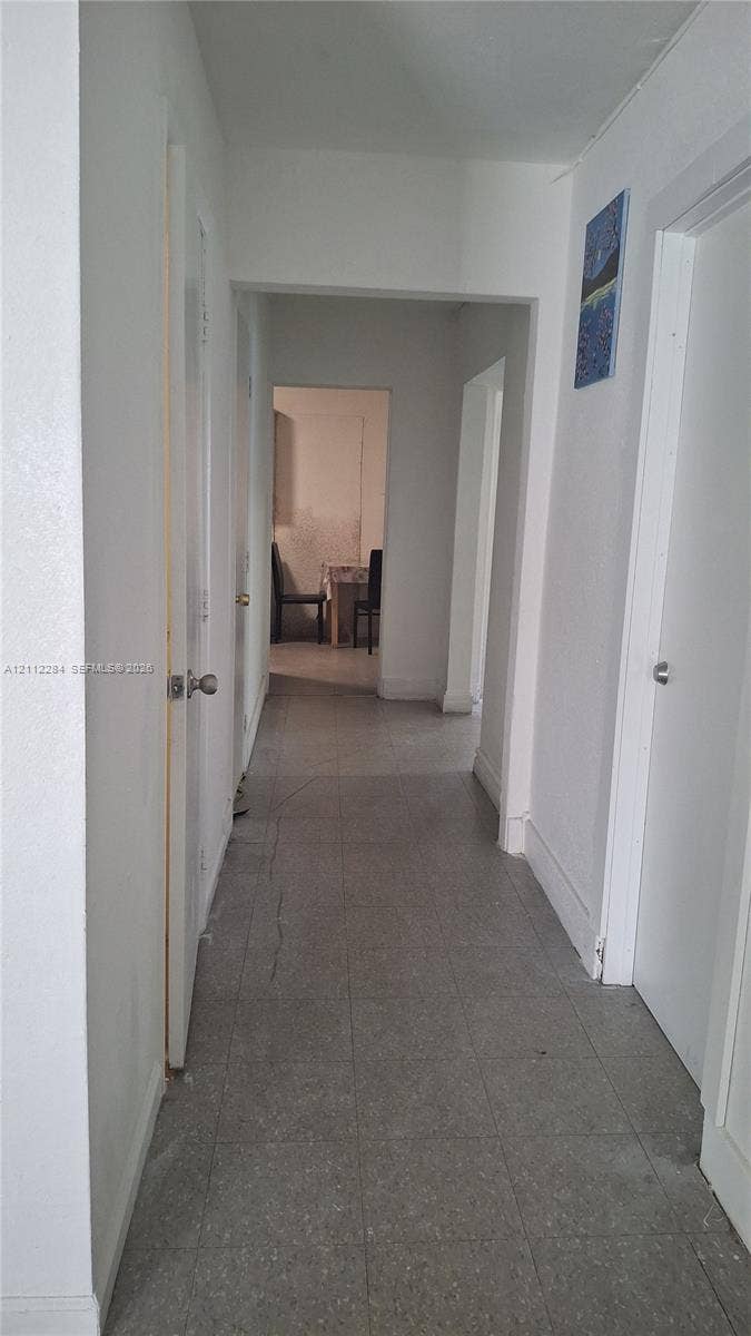 Interior hallway featuring neutral walls, white doors, and grey tile flooring