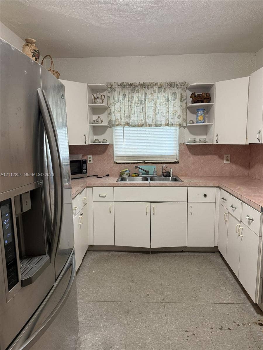 Kitchen featuring white cabinetry with open shelving, stainless steel refrigerator, solid-surface countertops, and dual-basin stainless steel sink