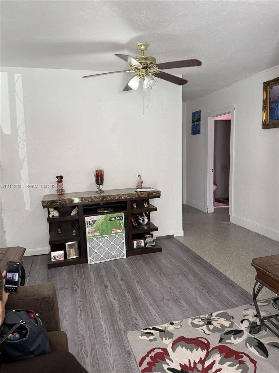 Interior space featuring grey wood-finish flooring and a multi-blade ceiling fan with an integrated three-light fixture
