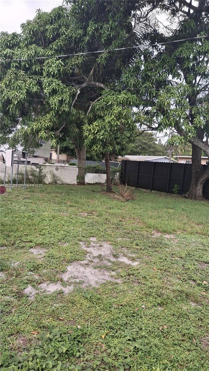 Spacious backyard featuring mature trees, a white masonry perimeter wall, and a dark-toned privacy fence