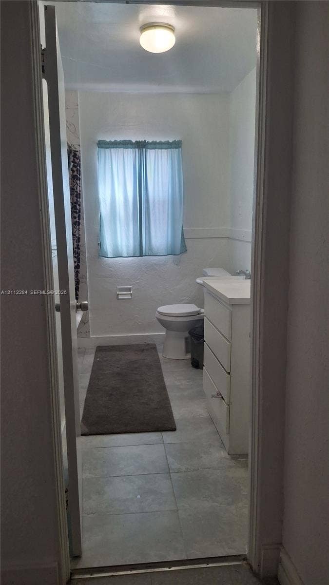 Bathroom featuring a white vanity cabinet, tiled flooring, a flush-mount ceiling light, and a window with a valance
