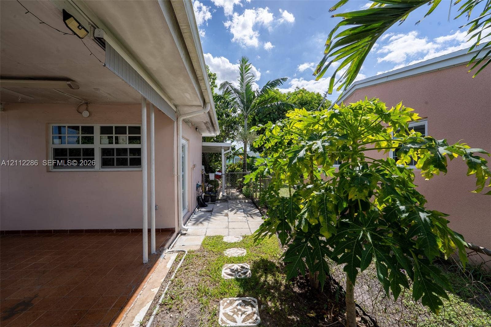 Covered patio with tiled flooring, concrete paver walkway, and exterior stucco finish
