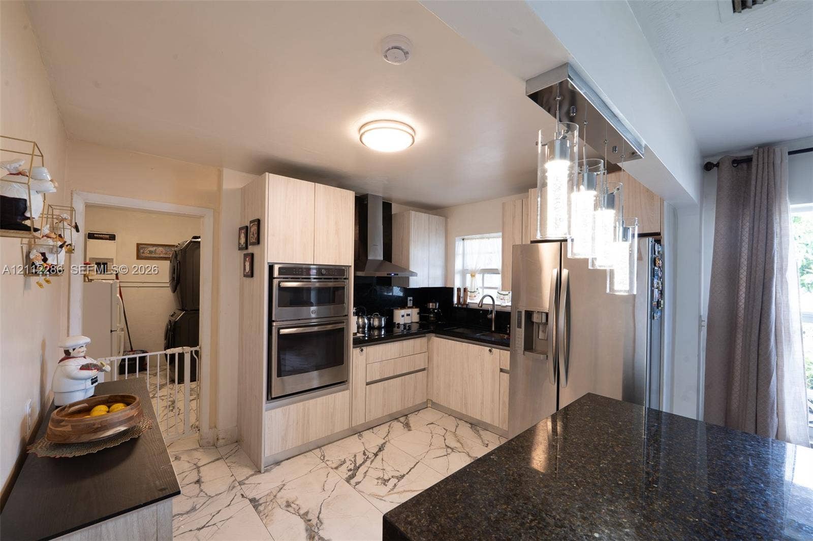 Kitchen featuring light-finish cabinetry, stainless steel double wall ovens, dark stone countertops, stone flooring with veining, and contemporary pendant lighting