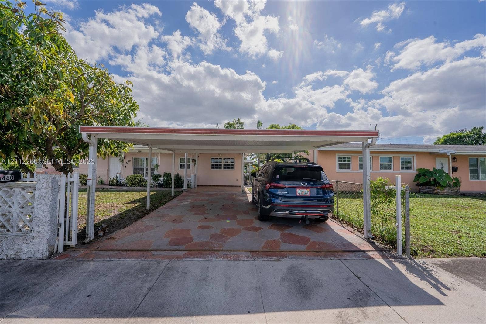 Covered carport featuring a decorative stone-paved floor and a concrete masonry unit fence