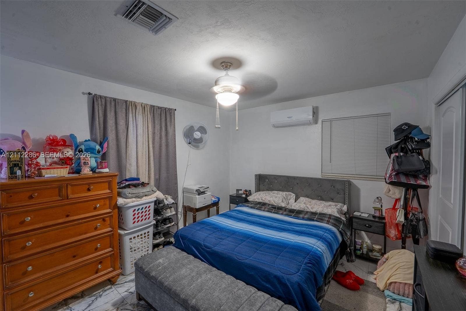 Room featuring stone-finish flooring, a wall-mounted ductless air conditioning unit, a central ceiling fan with an integrated light fixture, and horizontal window blinds
