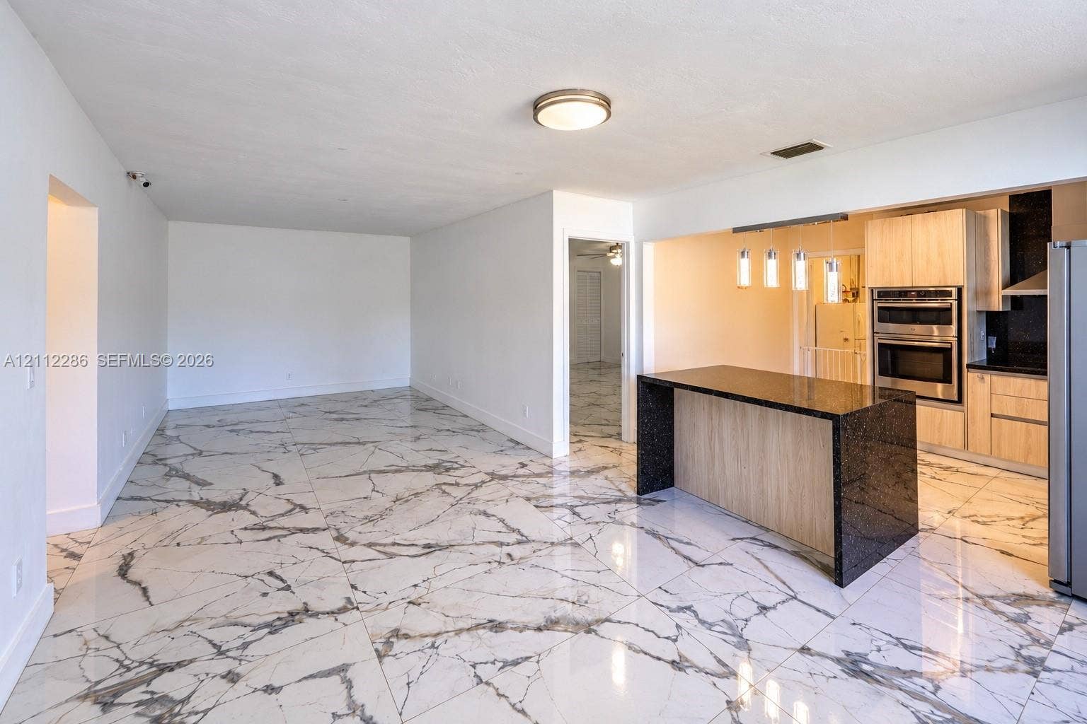 Large-format tile flooring, kitchen island with stone countertop, built-in double wall oven, contemporary pendant lighting, and flat-panel cabinetry