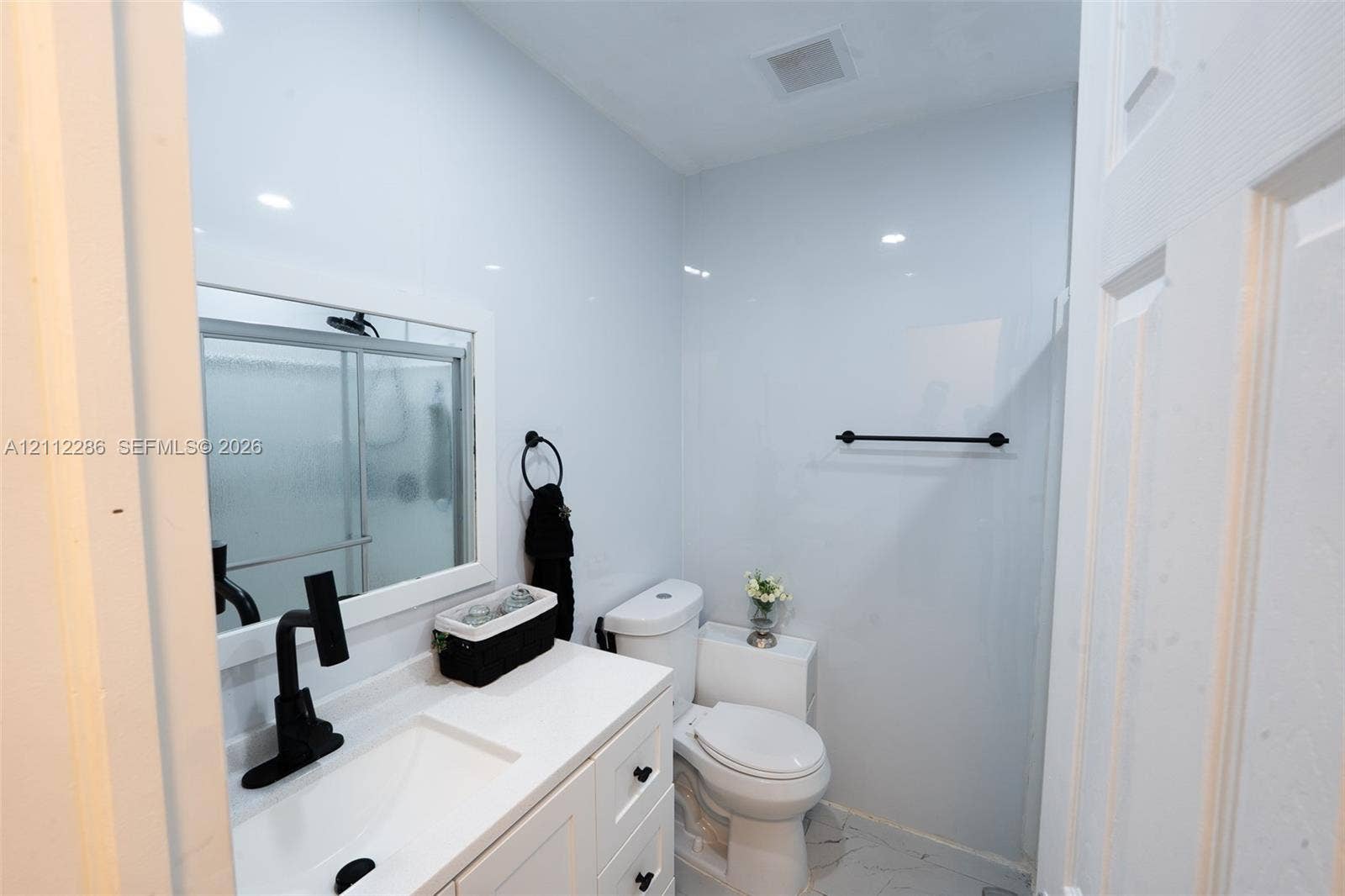Bathroom featuring a white vanity cabinet with an integrated sink, matte black faucet, framed mirror, and tile wall surfacing