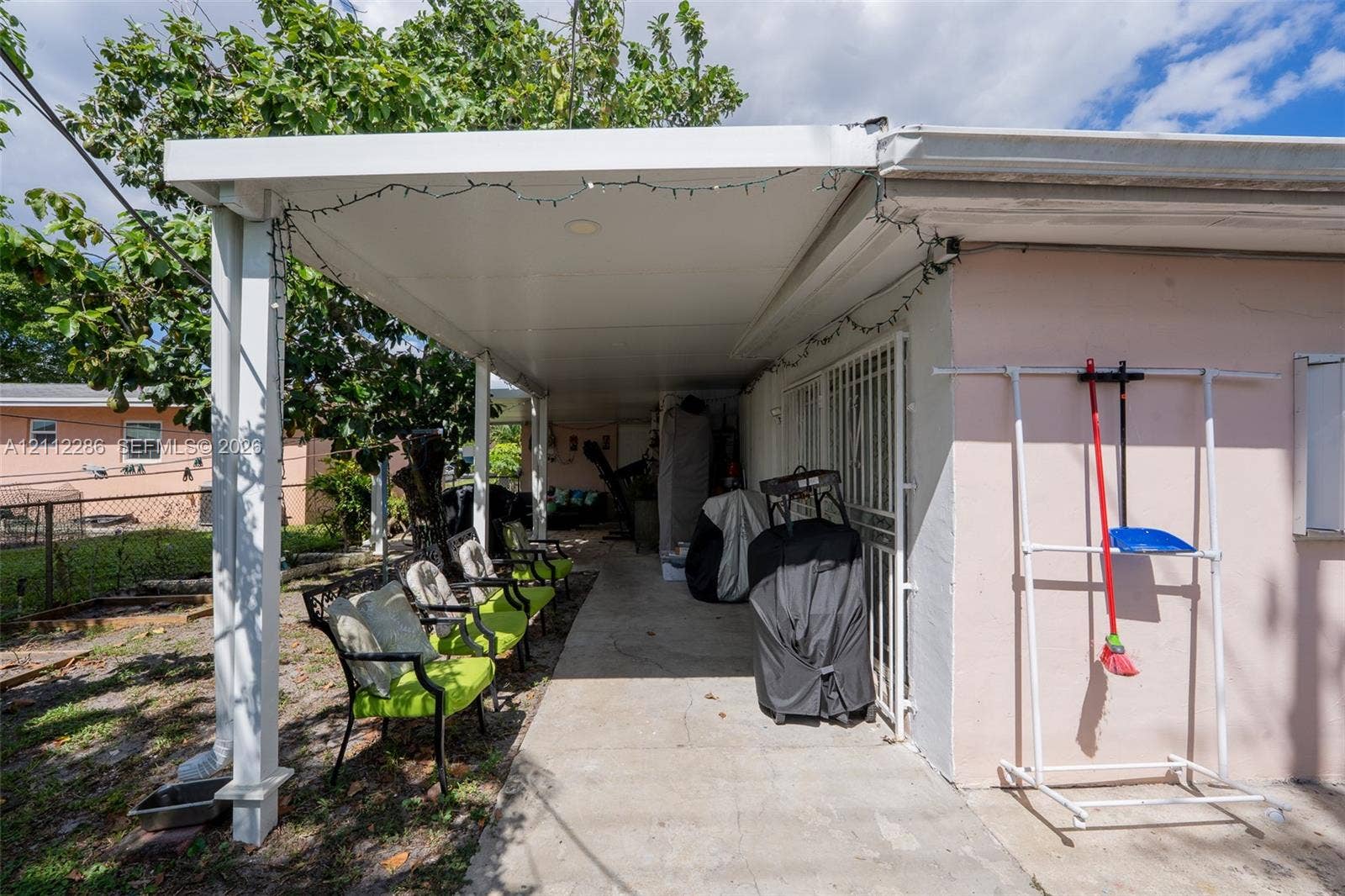 Covered exterior patio featuring a concrete floor, support pillars, and metal security bars over the exterior door